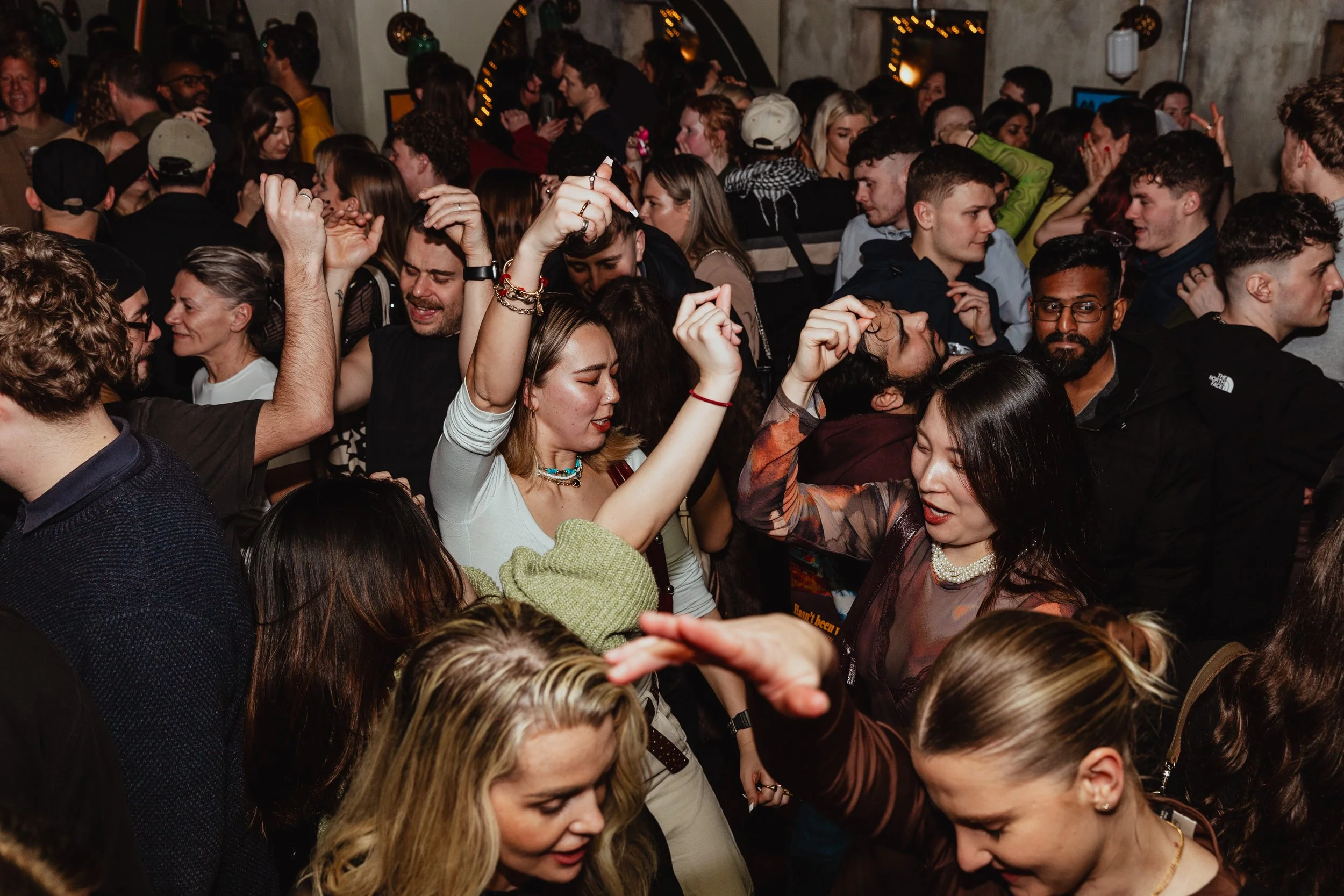 People dancing and enjoying music at a crowded indoor party or club with dim lighting and festive atmosphere.