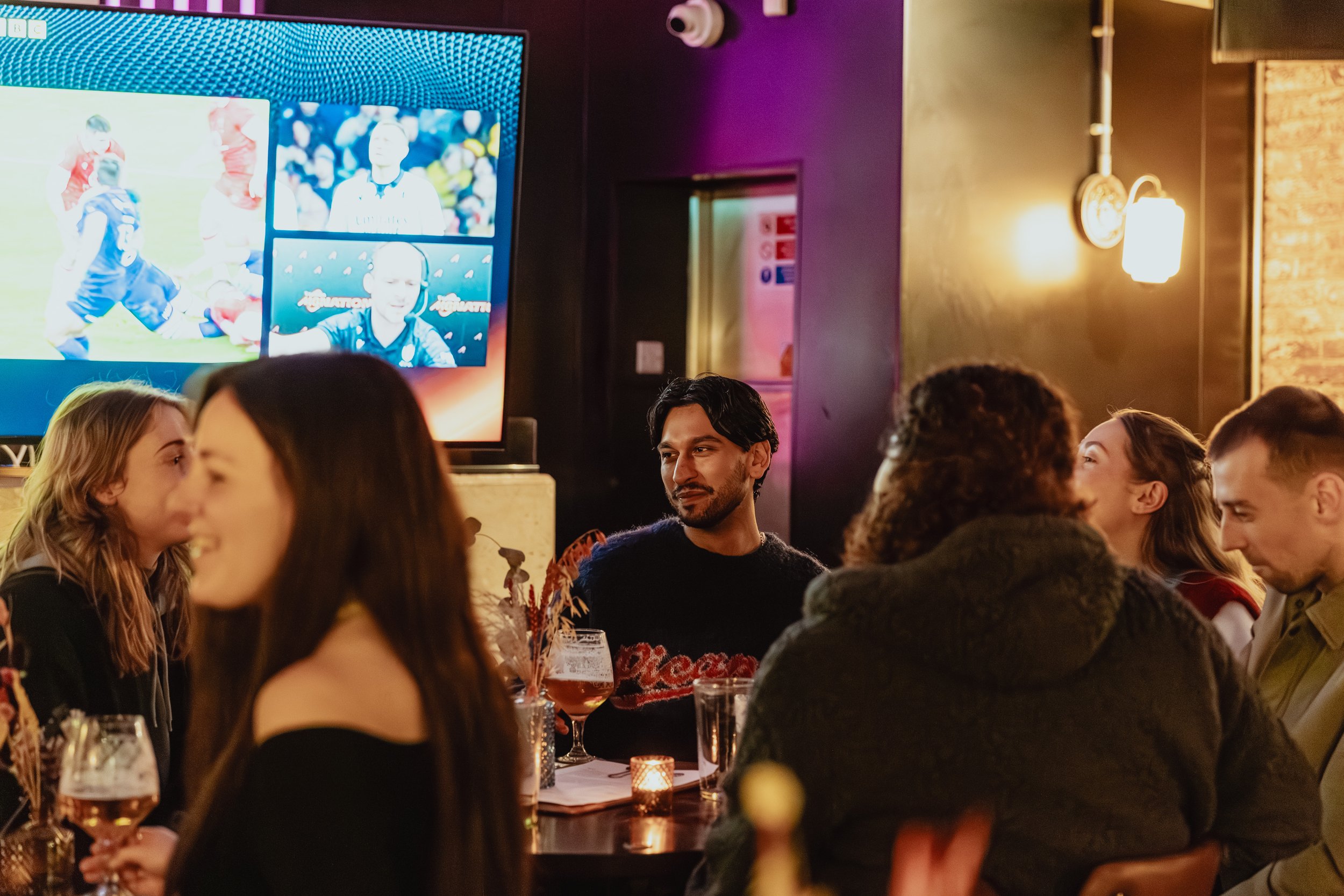 People sitting around a table in a bar or restaurant, watching sports on a large screen TV.