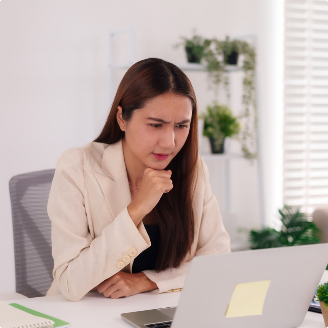 A woman with long brown hair sitting at a desk, looking confused or concerned at her laptop.