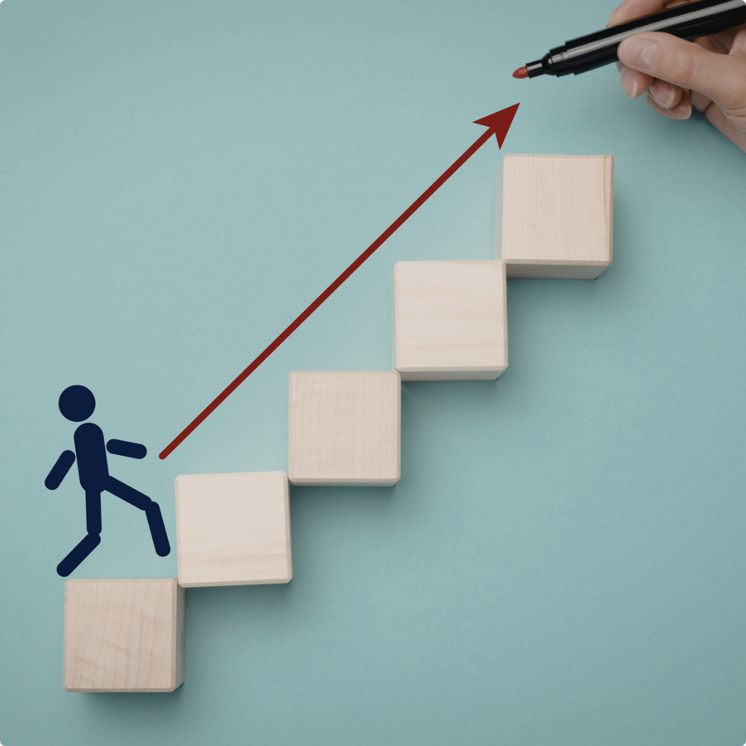 Wooden blocks arranged in increasing height to resemble ascending steps, with a hand drawing an upward arrow with a black marker, and a stick figure icon climbing the blocks symbolizing progress and growth.
