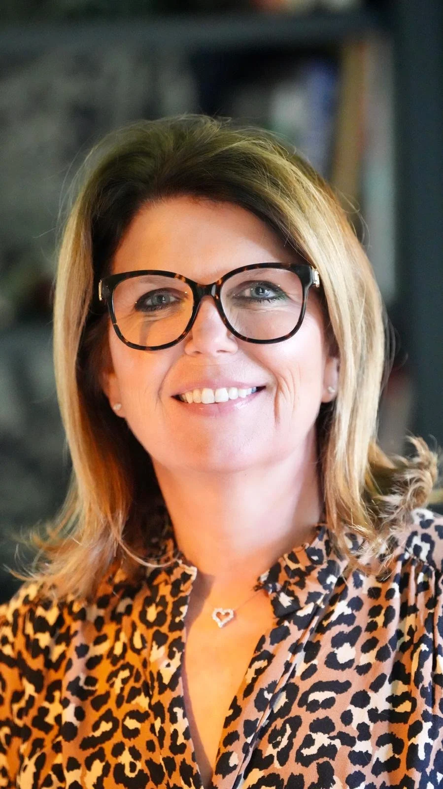 Smiling woman with blonde hair, glasses, and leopard print blouse.