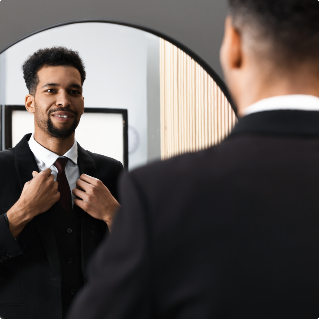 A man adjusting his suit tie while looking at himself in a mirror.