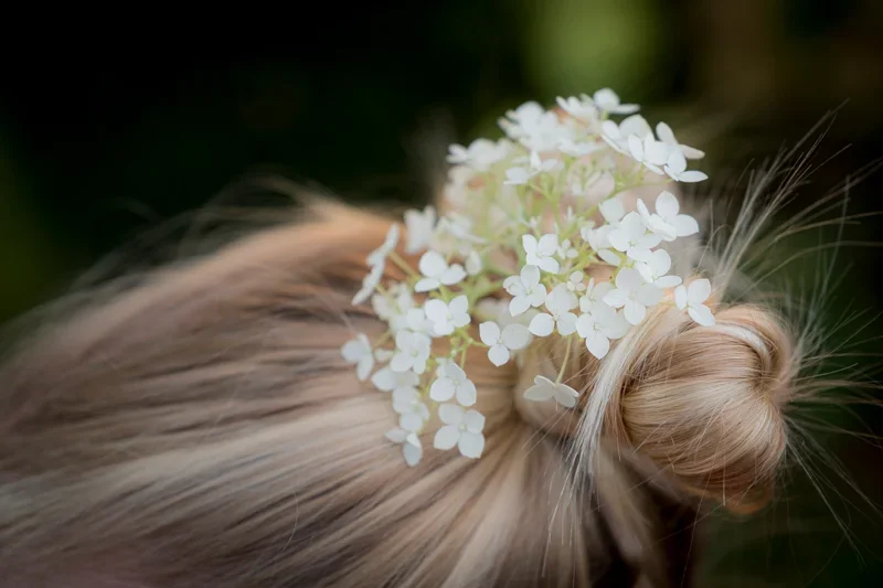 Blonde haren met een witte bloemenkrans in een paardenstaart.