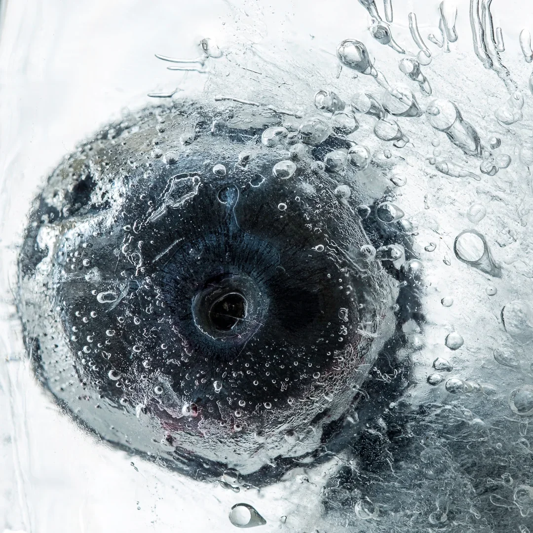 Close-up van een blauwe bes of bosbes die onder koud water of in ijs met druipers en bubbels is geplaatst.