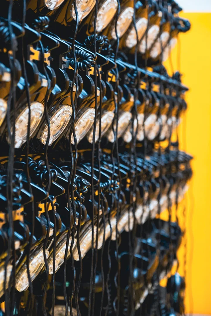 Kunstwerk gemaakt van vele oude telefoontoestellen georganiseerd op een muur met een gele achtergrond.