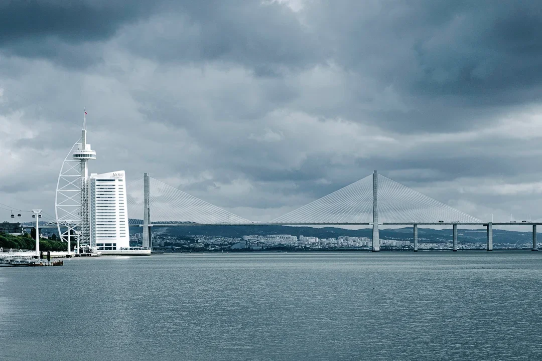 Stad met een modern kantoorgebouw en een grote brug over het water onder een bewolkte hemel.