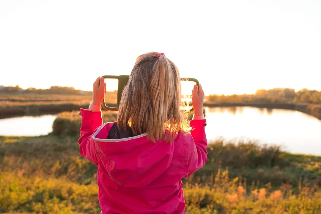 Een meisje in een roze jas neemt een foto met haar smartphone van een rivier in de natuur tijdens zonsondergang.