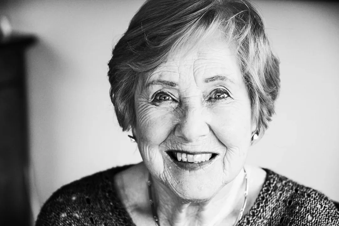 Portret van een lachende oudere vrouw met korte, blonde haar, in een zwart-wit foto.
