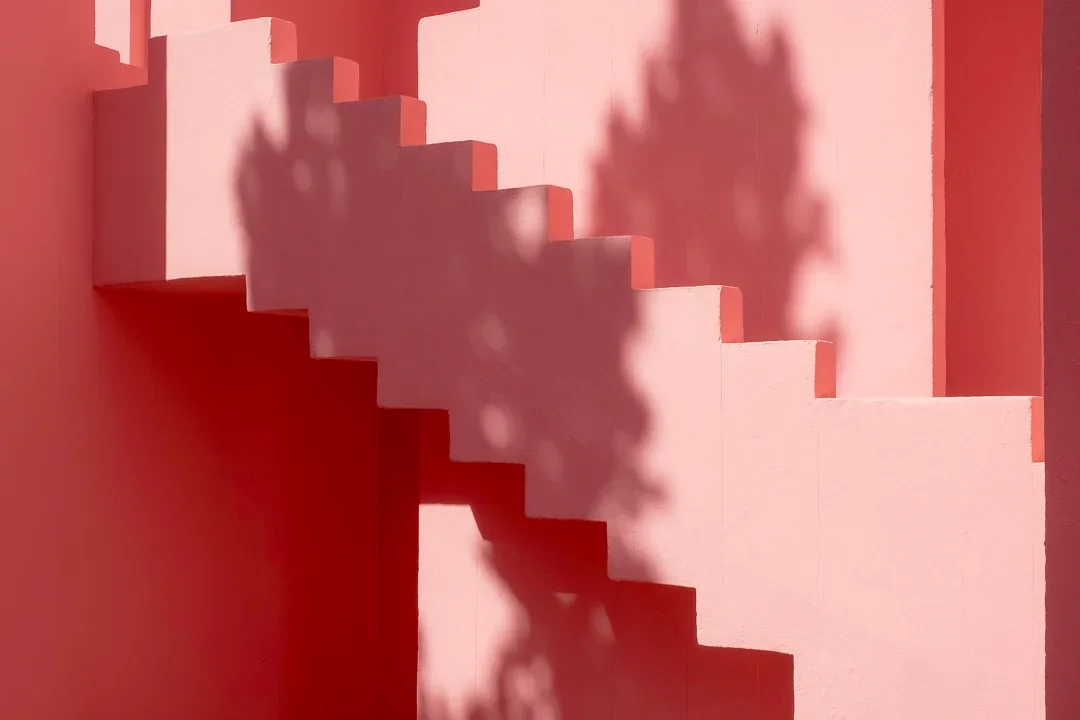 Een trap in een roze muur met een schaduw van een boom erop.