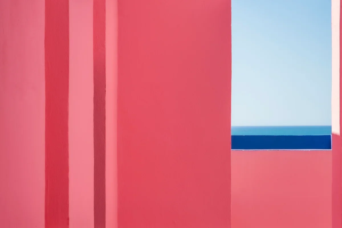 Een muur met roze en blauwe kleuren, met een raam dat uitkijkt op de zee.