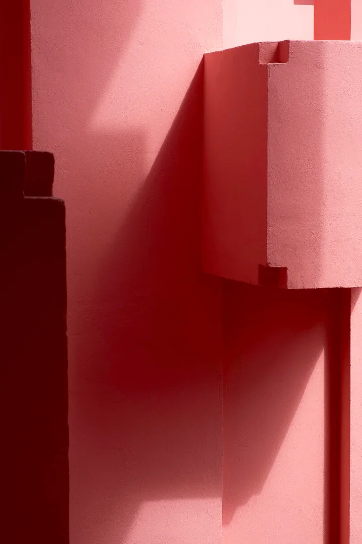 Een abstracte kunstinstallatie met voornamelijk roze en roodkleurige geometrische vormen en schaduwen.