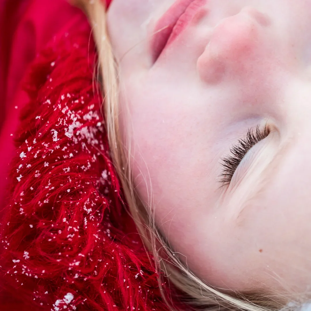 Close-up van een slapende jonge meisje met lichte huid en blonde haar, met een rode sjaal met sneeuwvlokken.