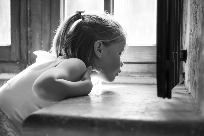 Een jonge meisje kijkt vol verwondering in een hoek van vensterbank naar iets kleins, vermoedlijk een insect, in zwart-wit