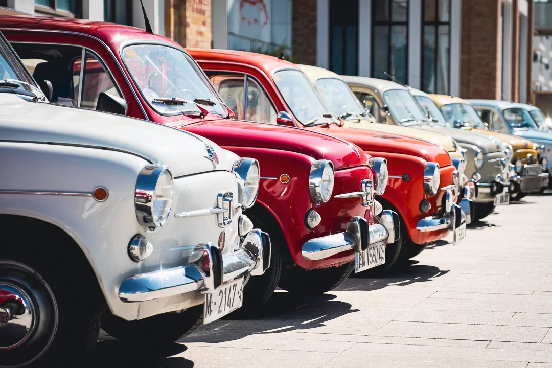 Een rij vintage auto's geparkeerd op straat, diverse kleuren zoals wit, rood, beige en blauw.
