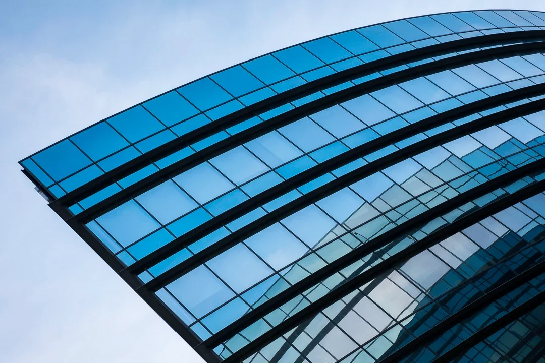 Hoog gebouw met een moderne glazen gevel dat tegen een blauwe hemel ligt.