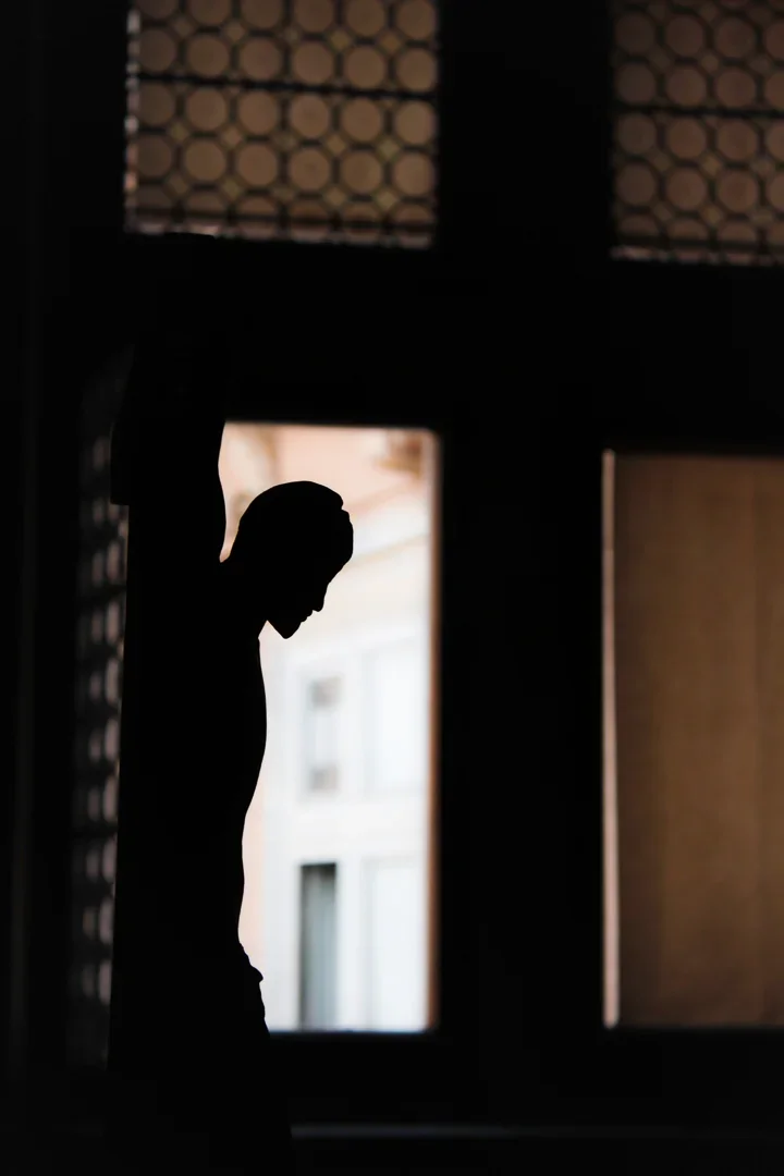 Silhouet van figuur van Jezus op een kruis die naar beneden kijkt binnen een kamer met ramen