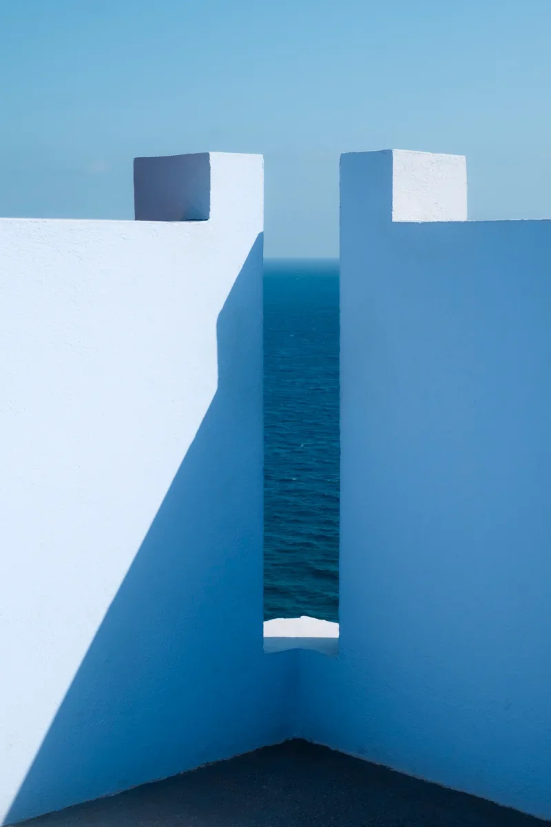 Lichbtblauwe muren met harde schduwen erop en een zeezicht tussen de muren.