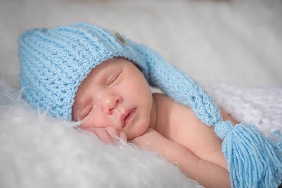 Zachte close-up van een slapend pasgeboren baby met een bontknoop en een blauwe wenspet