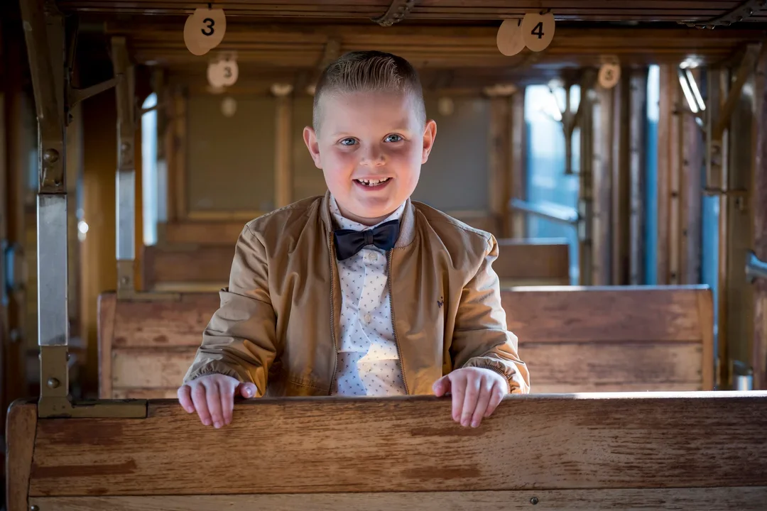 Lachende jongen in de trein, zittend op een houten bankje.
