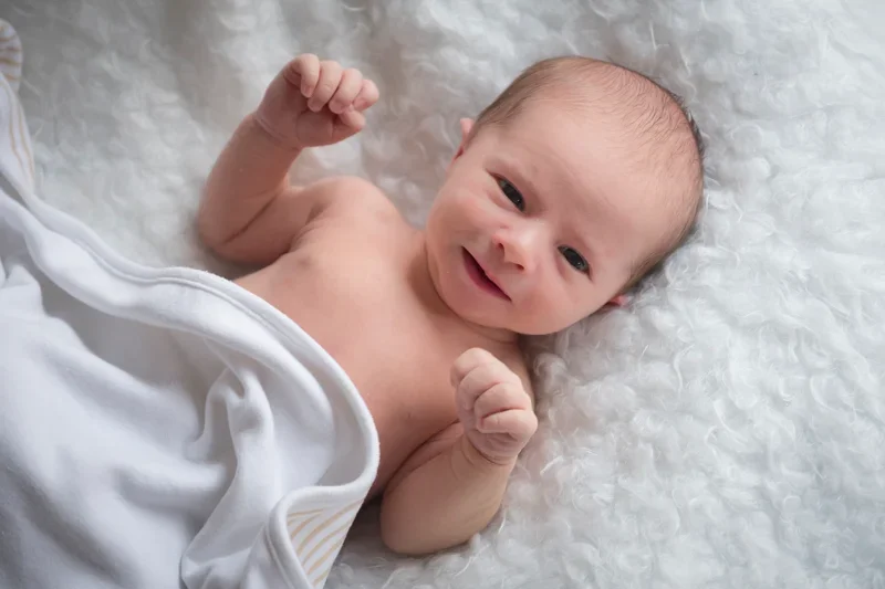 Lachend pasgeboren baby met opgetrokken armen, op een witte, zachte achtergrond.