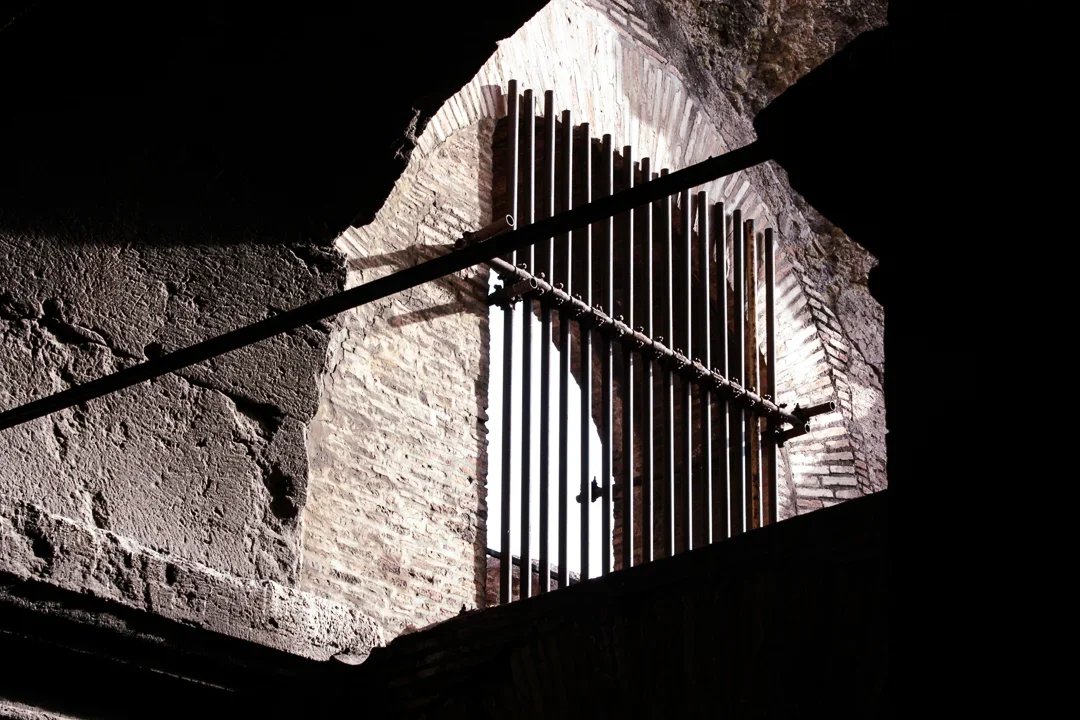 Een view vanaf beneden op een klein raam met een metalen hek, ingebouwd in een oude stenen muur, binnen een kasteel of oud gebouw, vermoedelijk Colosseum in Rome.