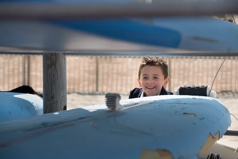 Een jonge jongen die glimlacht tussen surfplanken op het strand.
