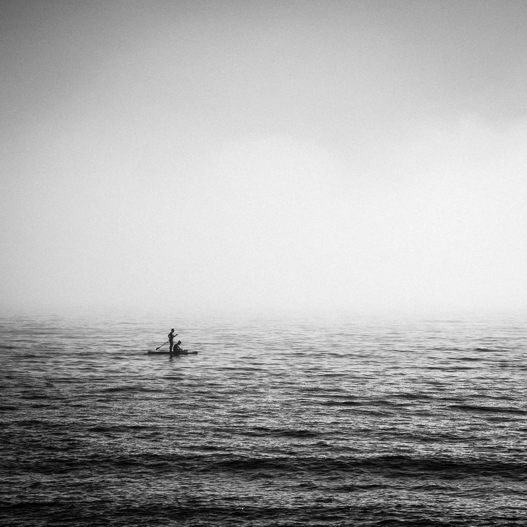 Twee mensen op een klein bootje op een rustige zee, zwart-wit foto, minimalistisch en mistig