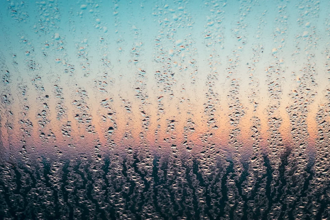 Regendruppels op een raampaneel met een wazige zonsondergang of zonsopgang op de achtergrond.