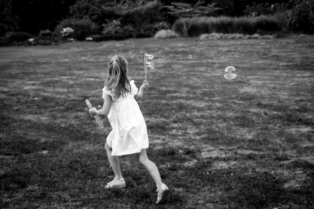 Een klein meisje in een witte jurk speelt met bellen in een grasveld.