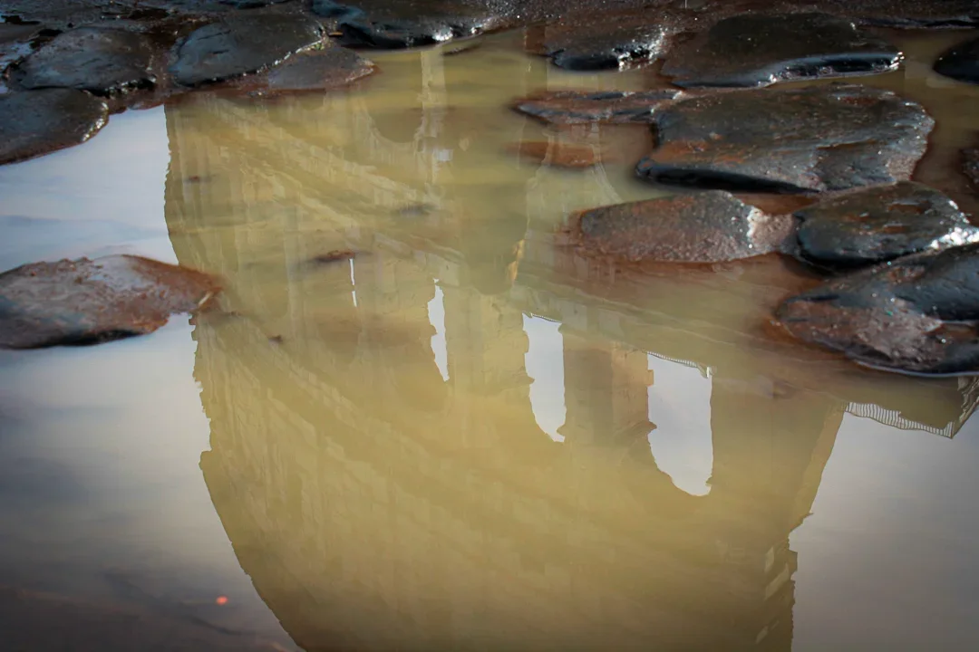 Reflectie van een gebouw Colosseum in Rome in een plas water met enkele stenen eromheen.