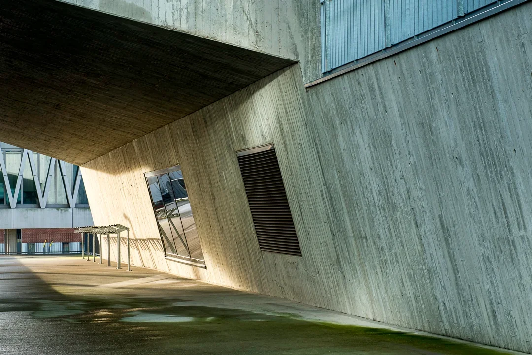 Moderne architectuur met schuine betonwanden en grote raampartijen op een stadsplein.