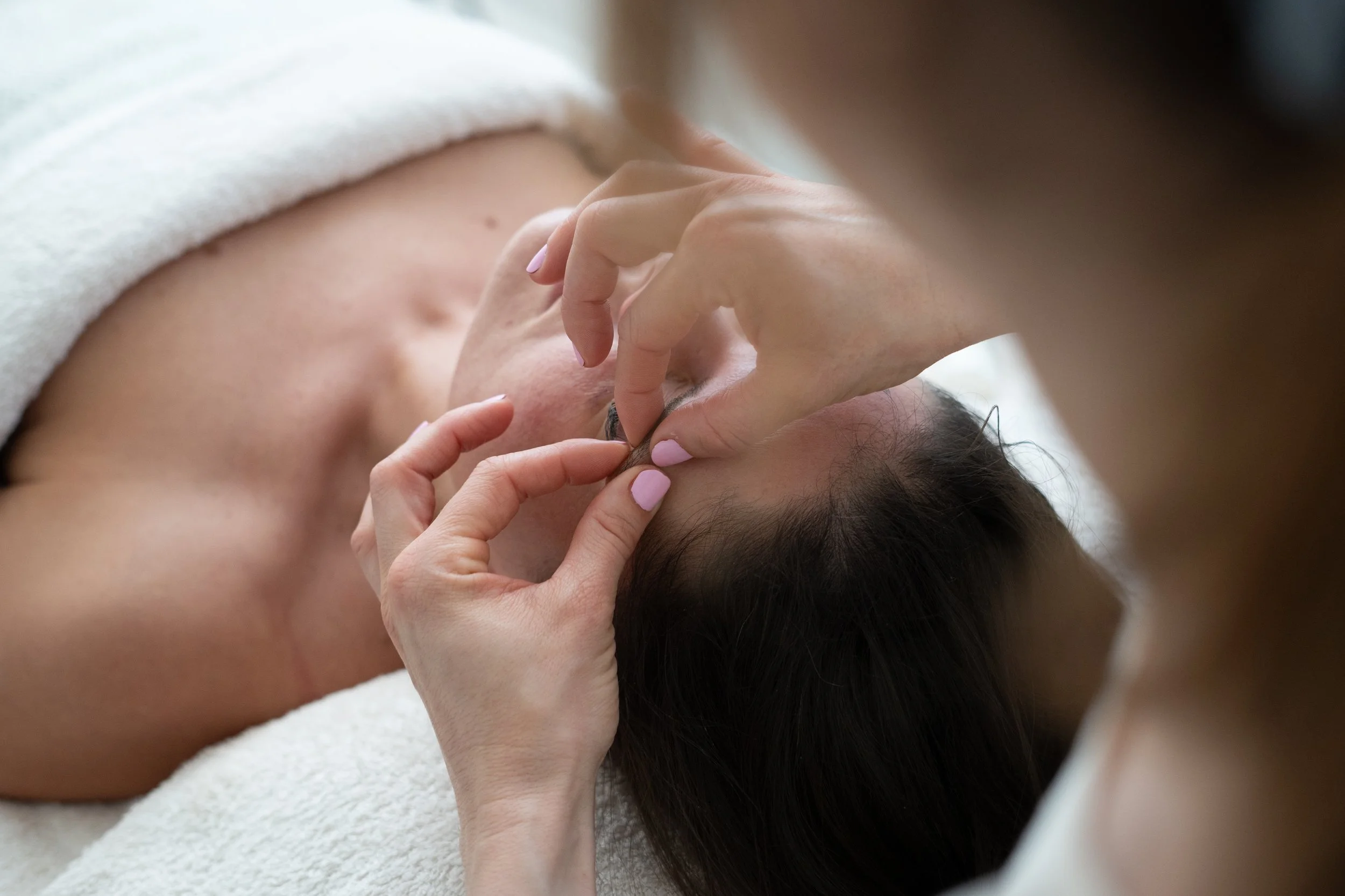 A person lying face down on a massage table, receiving a massage, with hands gently massaging their neck and shoulder area.
