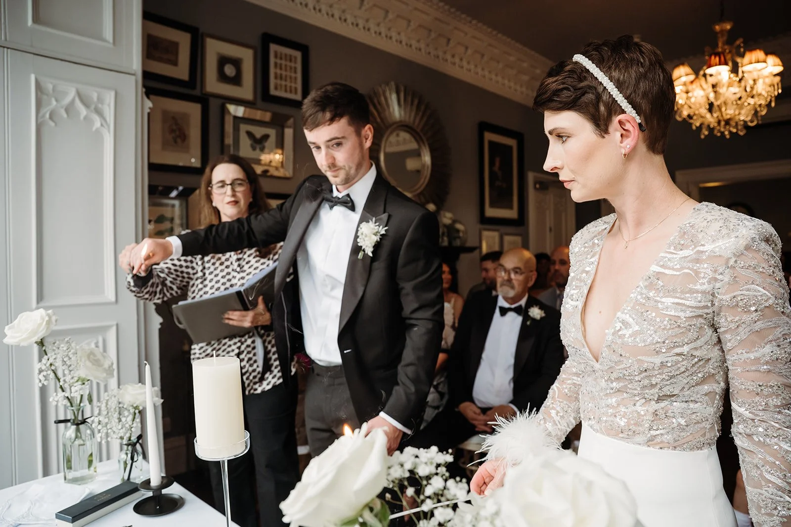 Bride and groom participating in a wedding ceremony with officiant in a decorated indoor setting, with seated guests in the background.