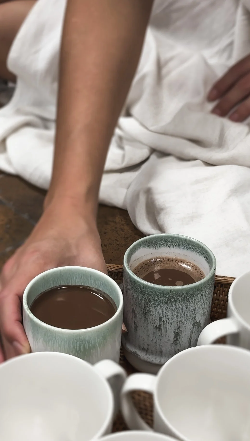 Personer holder kopper med varm chokolade eller kaffe, omgivet af flere kopper på et bord.