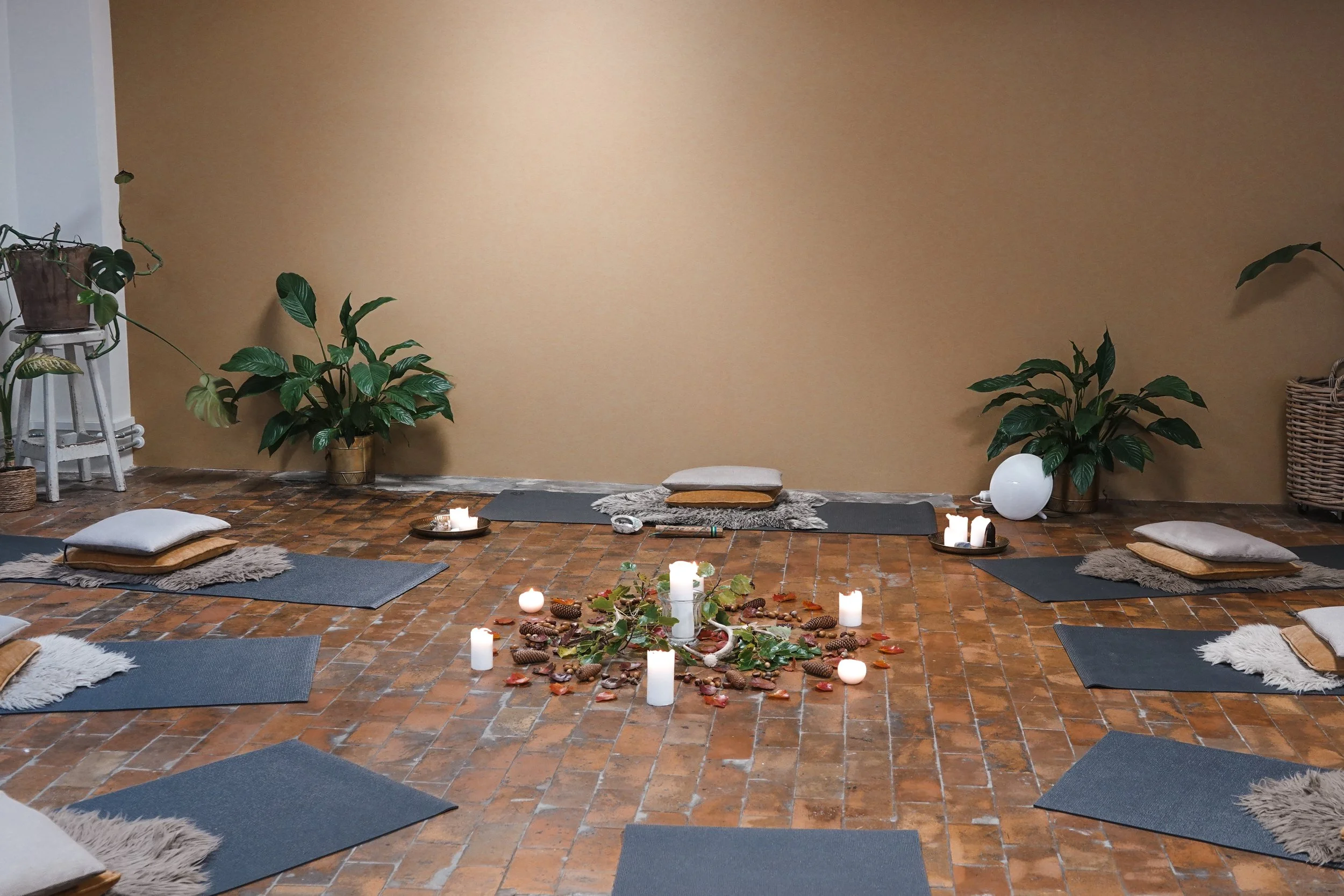 Indendørs yoga- eller meditationsrum med puder, lys, stearinlys og planter på brændte murstensgulve.