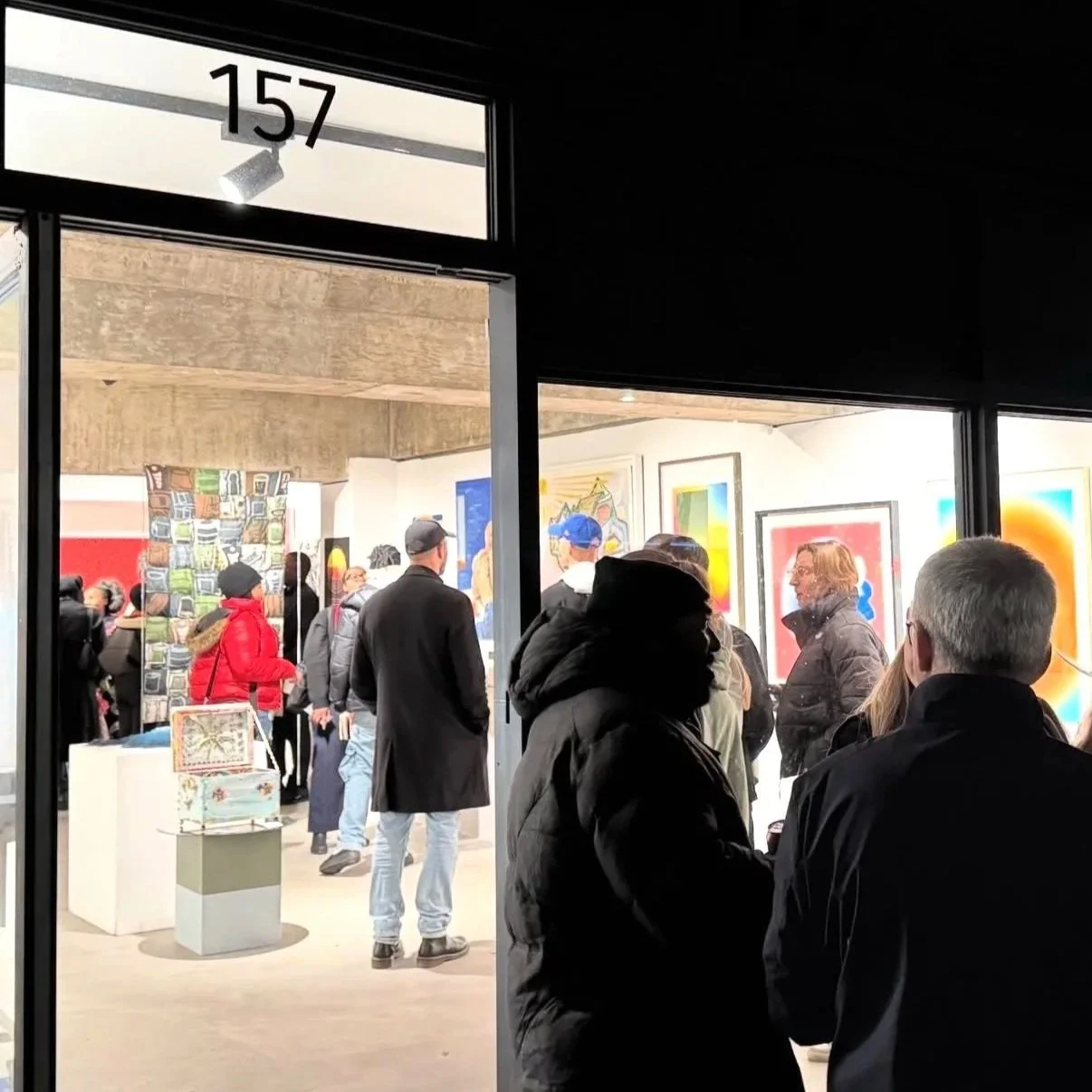 Tiago Caria, Exhibition View, 2026, photograph, gallery entrance with visitors viewing contemporary figurative artworks through glass, nighttime street context, conveying public engagement and psychological presence.