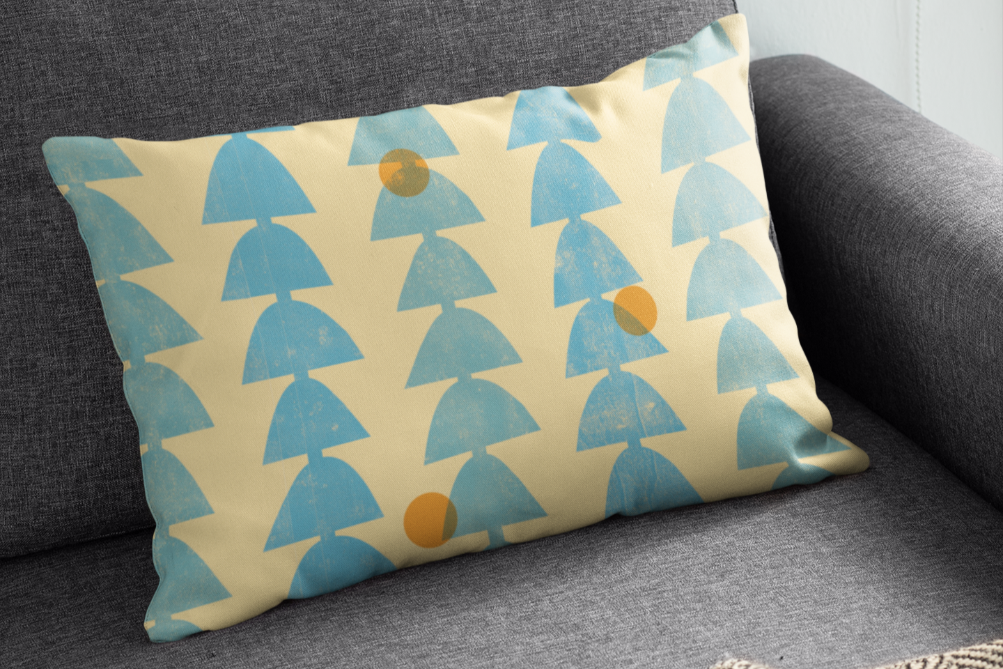 A rectangular cushion with a pattern of blue abstract shapes and orange circles on a cream background, placed on a dark gray sofa.