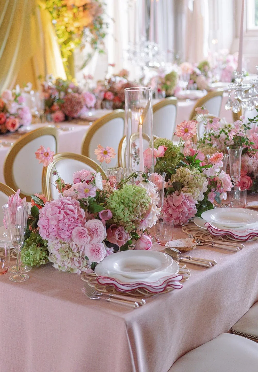 Elegant dining table decorated with pink and white flowers, candles, and fine china for a wedding or special event.