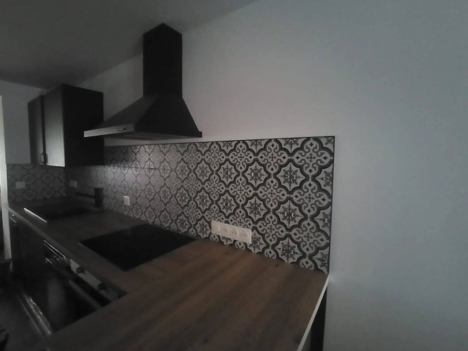 Cuisine moderne avec un plan de travail en bois, un mur avec carrelage décoratif noir et blanc, et une hotte aspirante noire.
