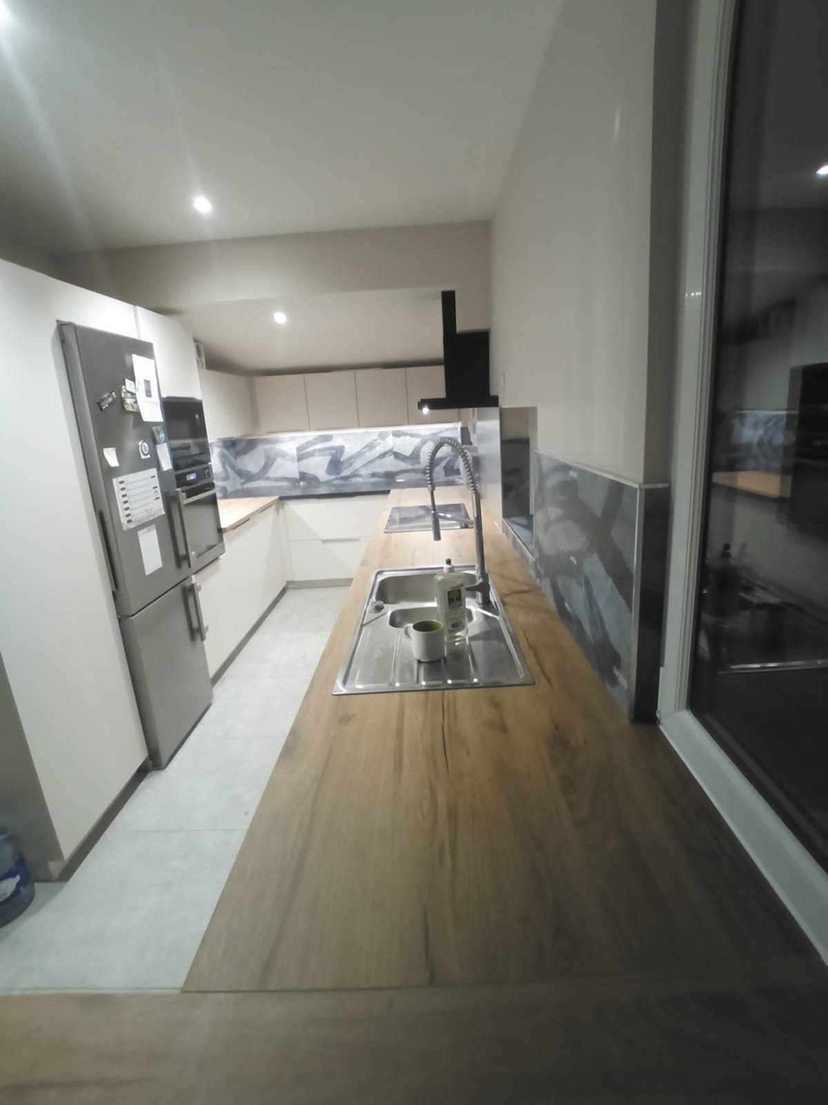 Cuisine moderne avec un plan de travail en bois, évier inox, réfrigérateur, four micro-ondes et plaque de cuisson, vue de l'angle.