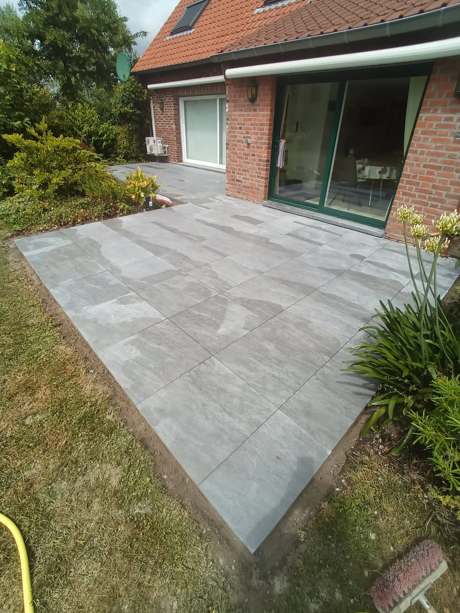 Terrasse en pierre grise devant une maison à briques avec de la végétation environnante.
