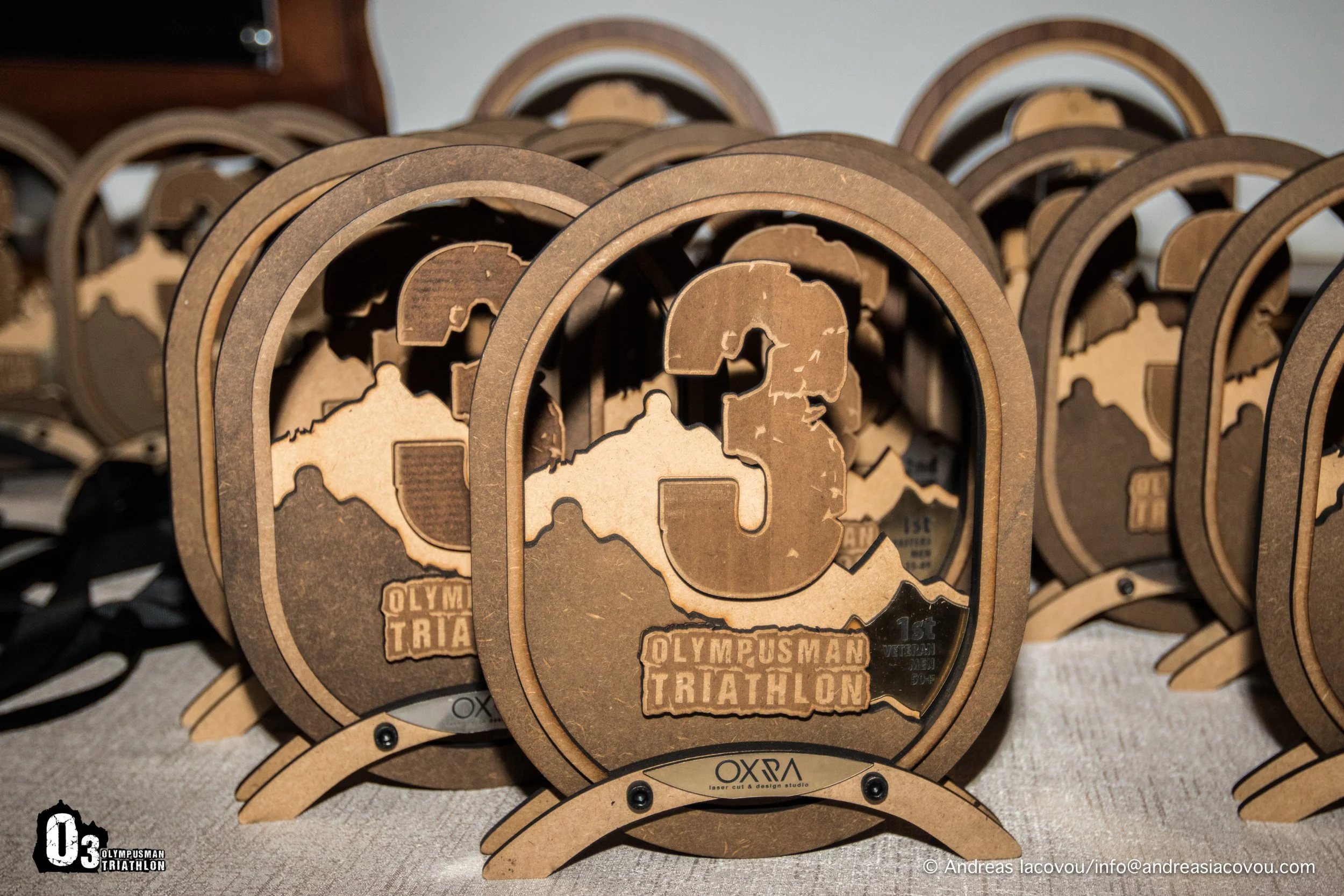 Wooden medals with a large number 3 and a map of Greece, labeled 'Olympus Man Triathlon' for the 15th veteran edition.