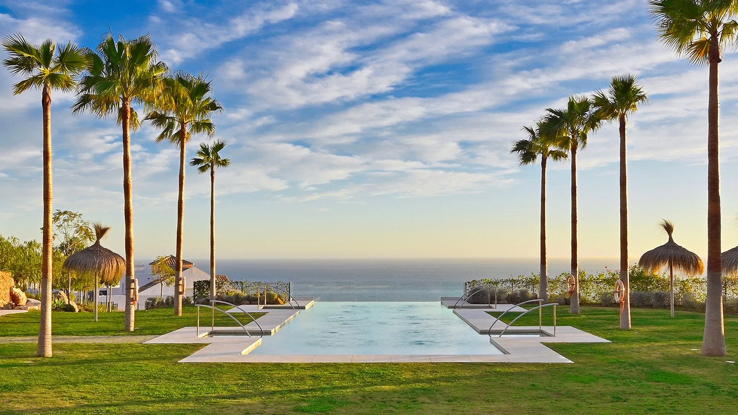 Piscina infinita en un resort con palmeras y vista al mar, bajo un cielo con nubes suaves