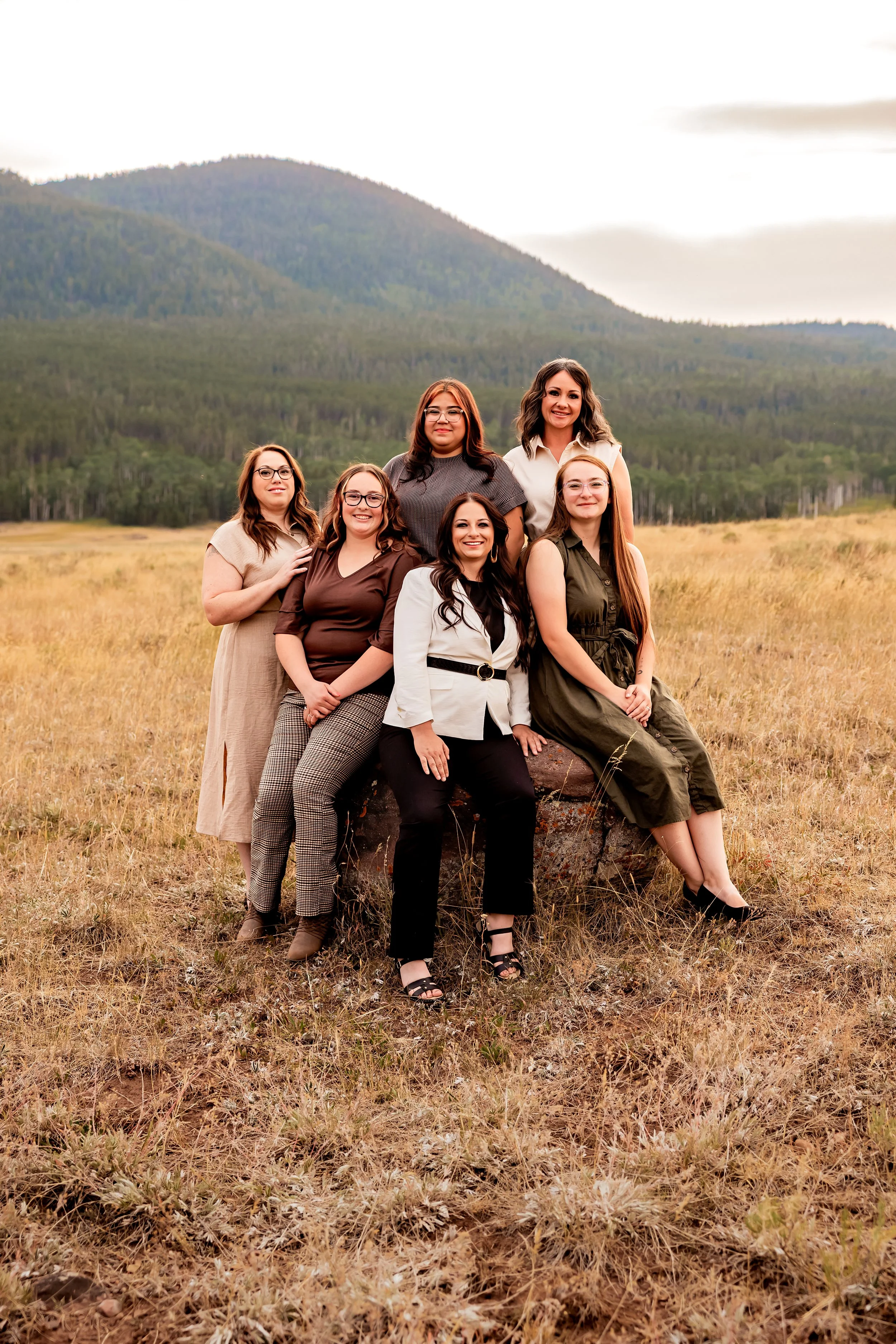 Six women posing outdoors in a field with mountains in the background.