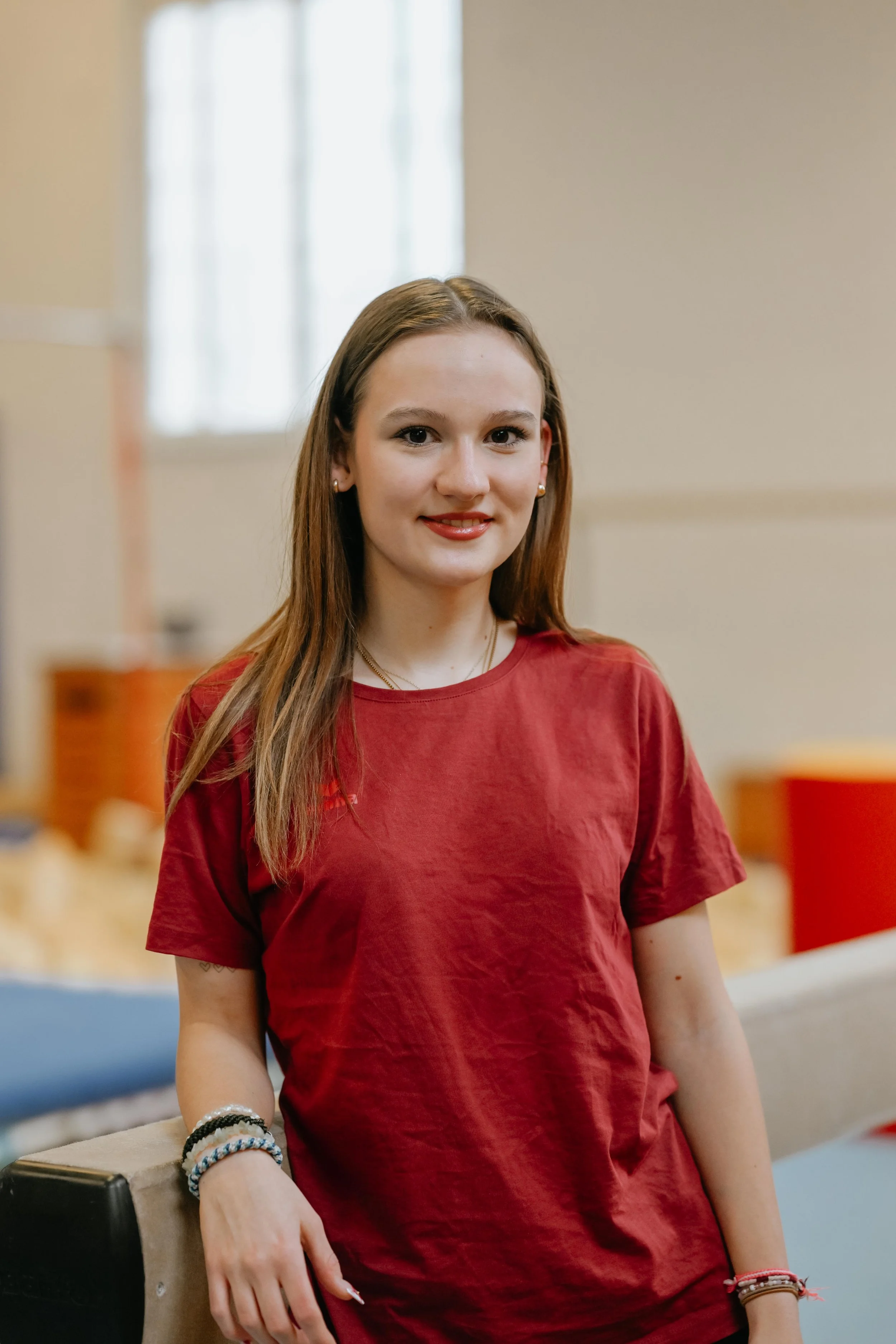 Junge Frau mit braunen Haaren in rotem T-Shirt steht in einem Raum, vermutlich in einer Halle oder im Veranstaltungsraum.