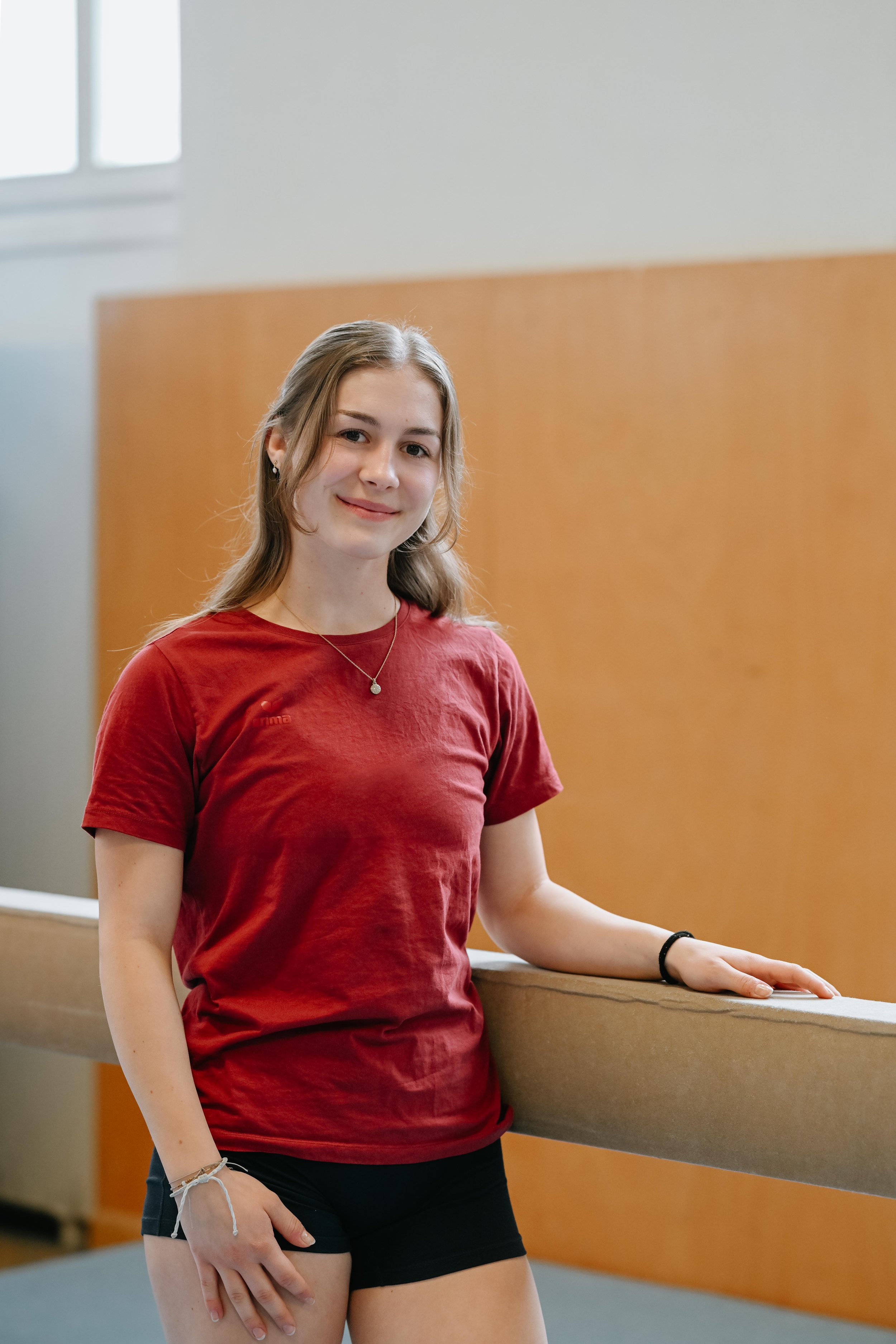 Junge Frau in rotem T-Shirt und schwarzen Shorts, die an einem Geländer im Innenraum steht.