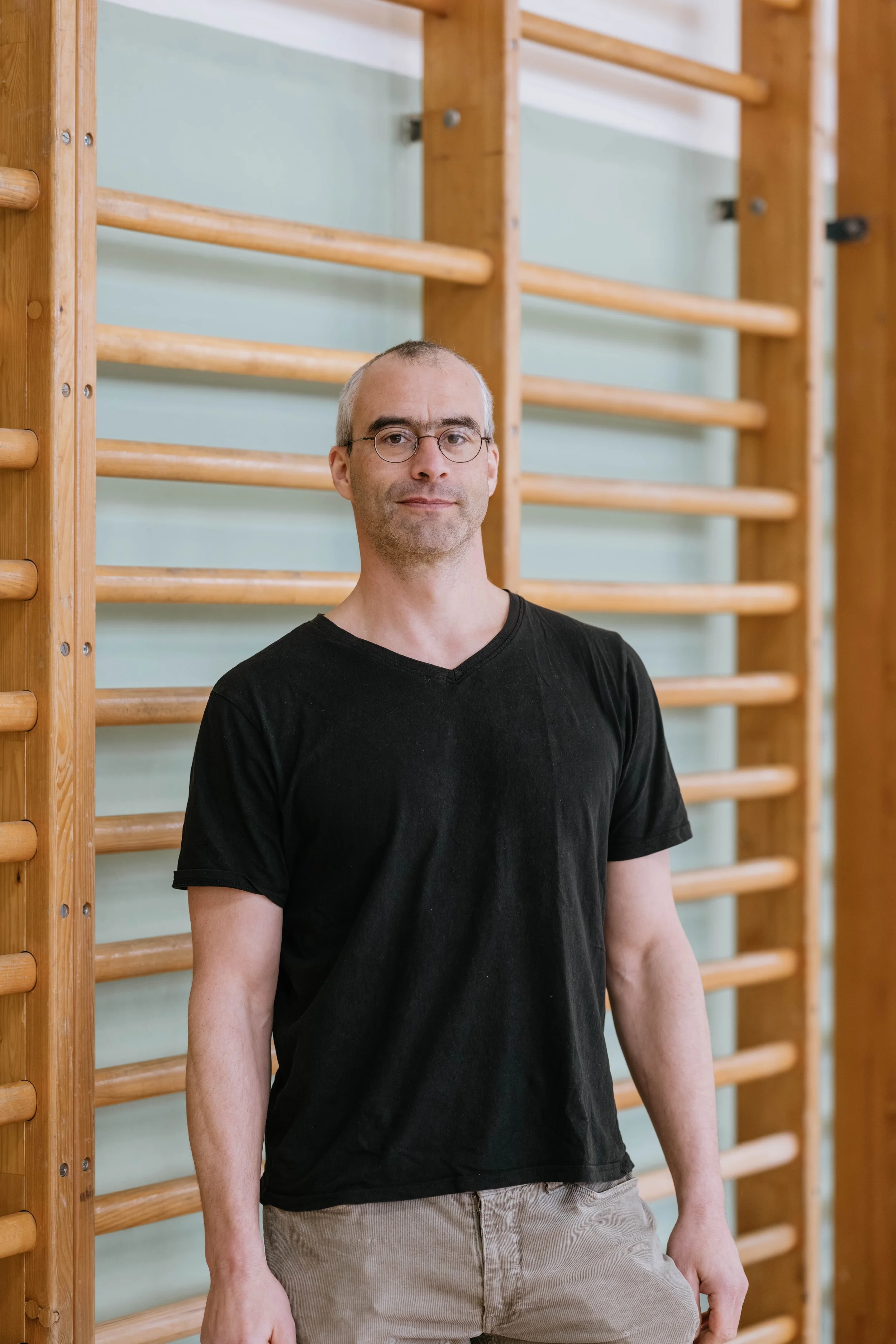 Mann steht an einer Wand mit Holztrainingsgeräten in einem Fitnessraum.