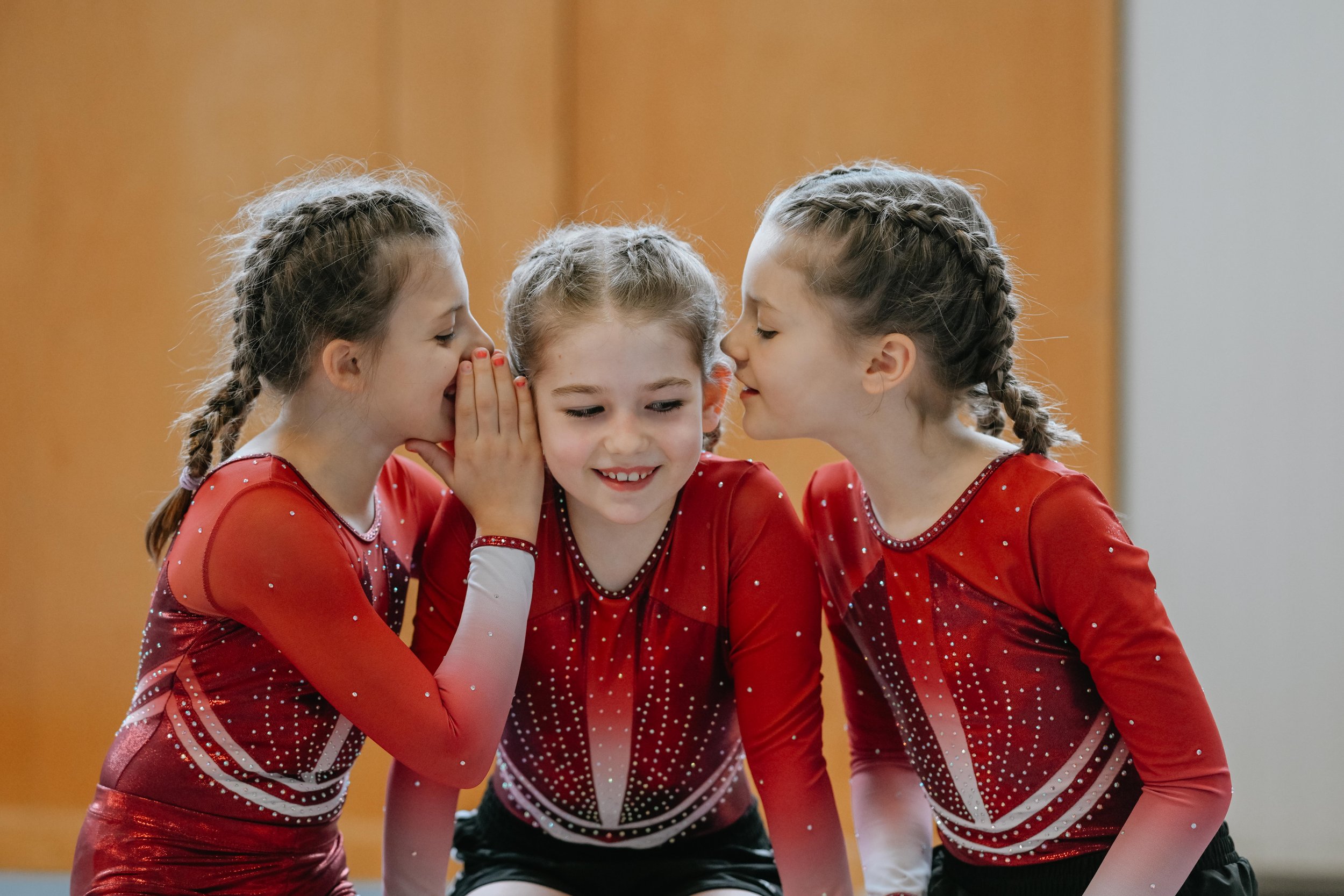 Drei junge Mädchen in roten Turnanzügen beim Flüstern und Reden.