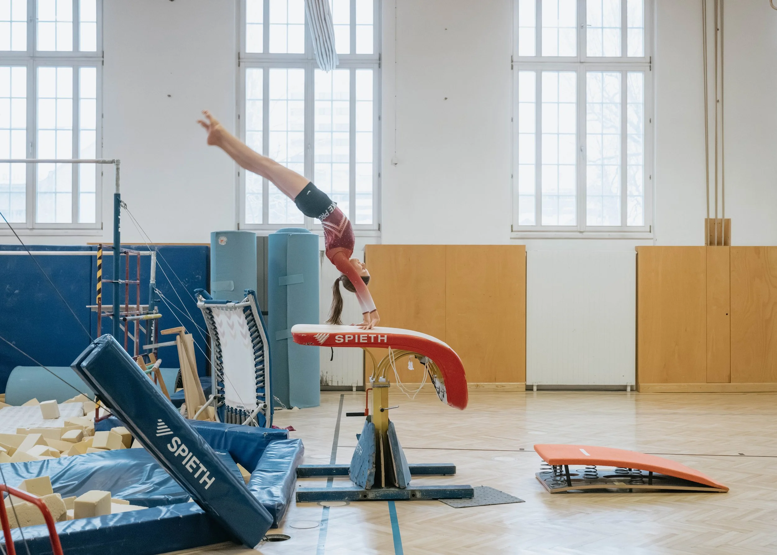 Ein junges Mädchen macht einen Handstand auf einem Turngerät in einer Turnhalle.