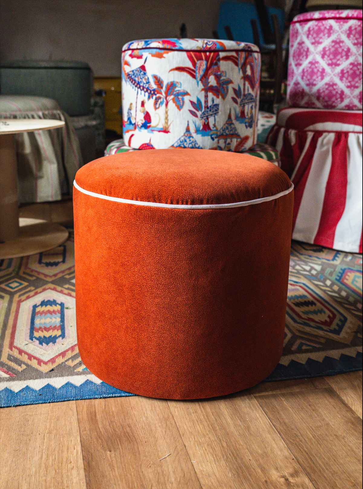A round, orange upholstered stool placed on a multicolored patterned rug.